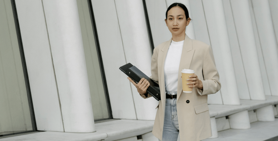 Professional woman walking through a modern office space holding a tablet and a coffee cup, representing a diverse workforce