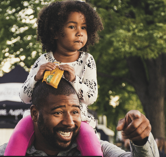 Smiling father giving his daughter a piggyback ride outdoors, enjoying playful time together in a park