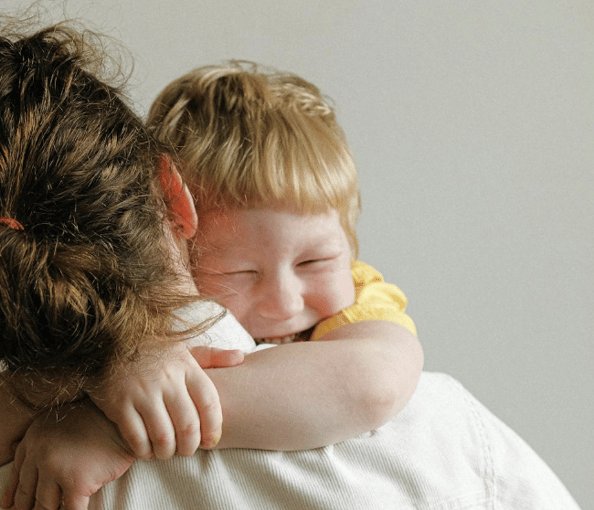 Smiling child hugging an adult, showing affection and emotional comfort in a warm, supportive environment
