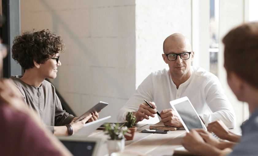 Diverse group of professionals in a tech office having a discussion around a table with digital devices