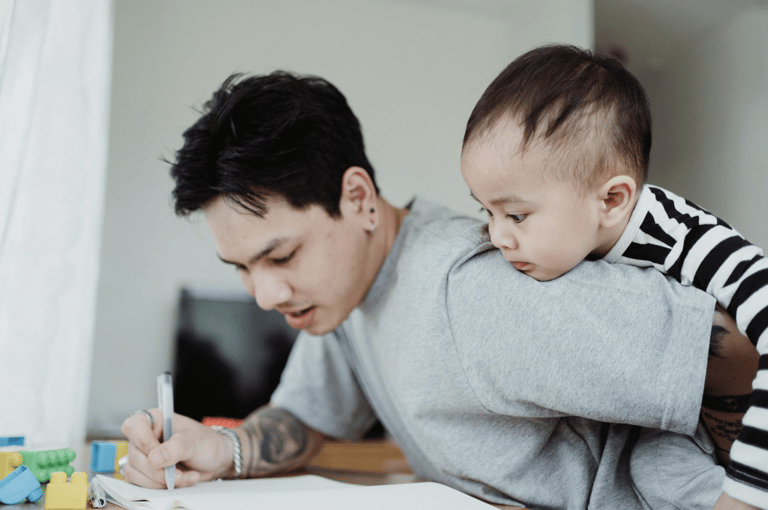 Father helping his young child with a drawing at a table, both focused and engaged in the activity