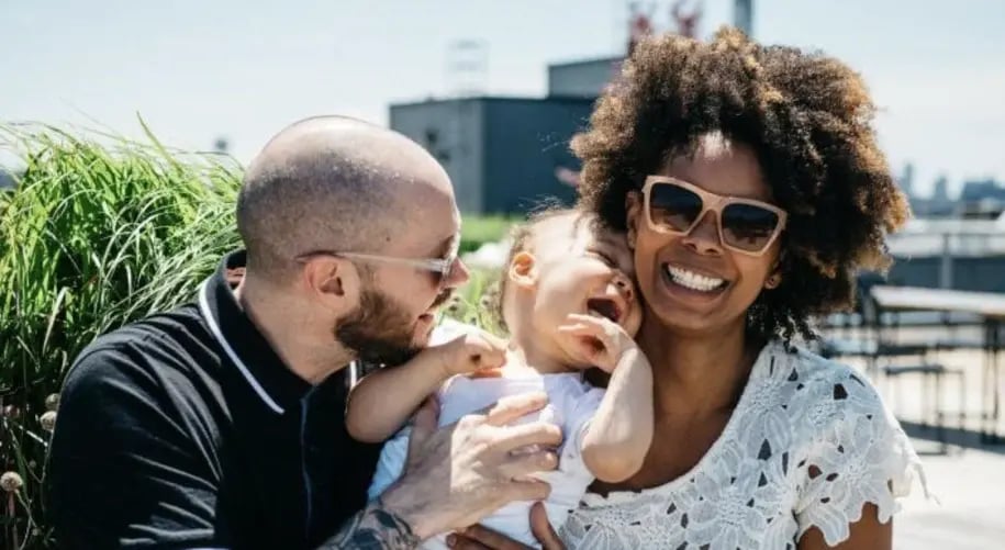 Couple smiling and holding their baby outdoors on a sunny day, enjoying a family moment