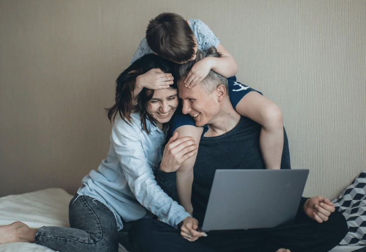 Smiling family sitting on a couch with a laptop, enjoying time together while managing responsibilities from home