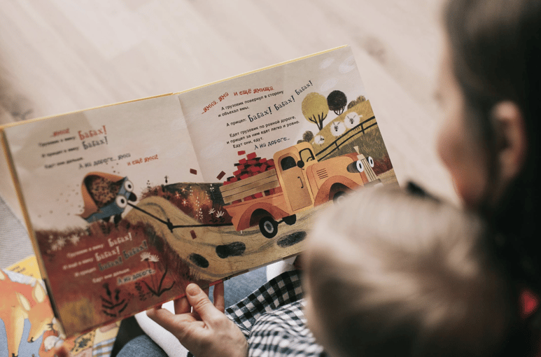 Adult reading a colorful picture book to a child, sharing a bonding moment through storytelling
