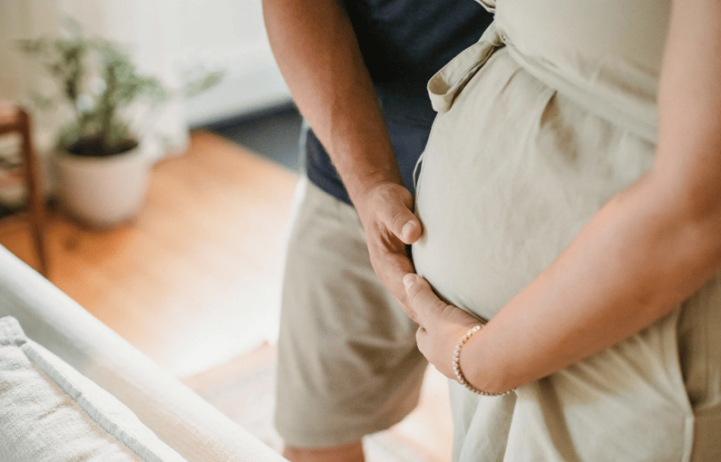 A close-up of a pregnant woman's belly with a person's hands gently touching it.