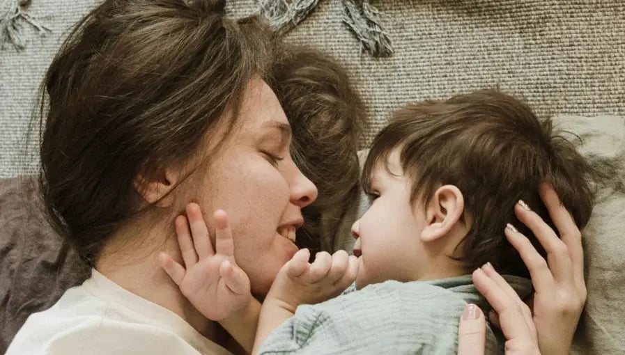 Mother and toddler lying face to face on a carpet, sharing a tender and affectionate moment