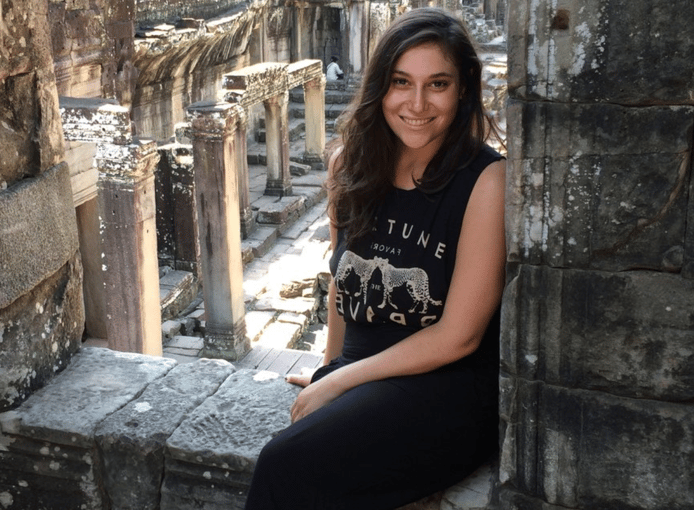 Woman sitting in front of ancient stone ruins, smiling and posing for a photo outdoors