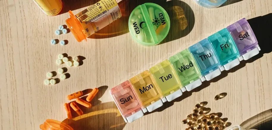 A seven-day pill organizer filled with various medications and capsules on a wooden table.