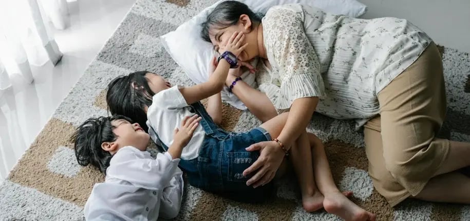 Mother lying on the floor with her two children, smiling and playing together in a relaxed home environment