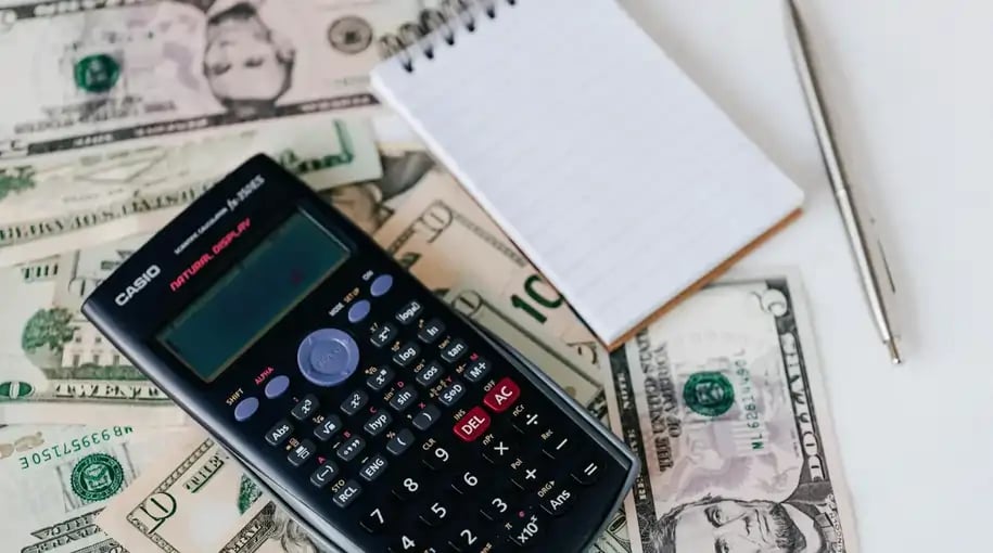Calculator, notebook, pen, and dollar bills on a table, symbolizing financial planning and budgeting