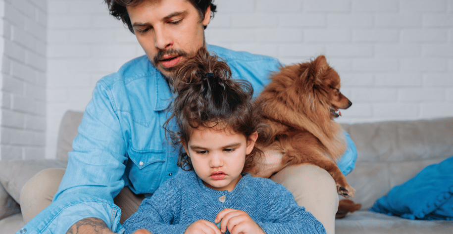 a father helping his daughter draw while holding the family dog