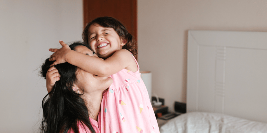 Daughter hugging her mom's face on the bed