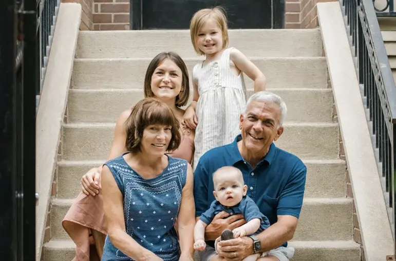 Family with young children sitting on outdoor steps, smiling and posing together for a photo during a difficult time