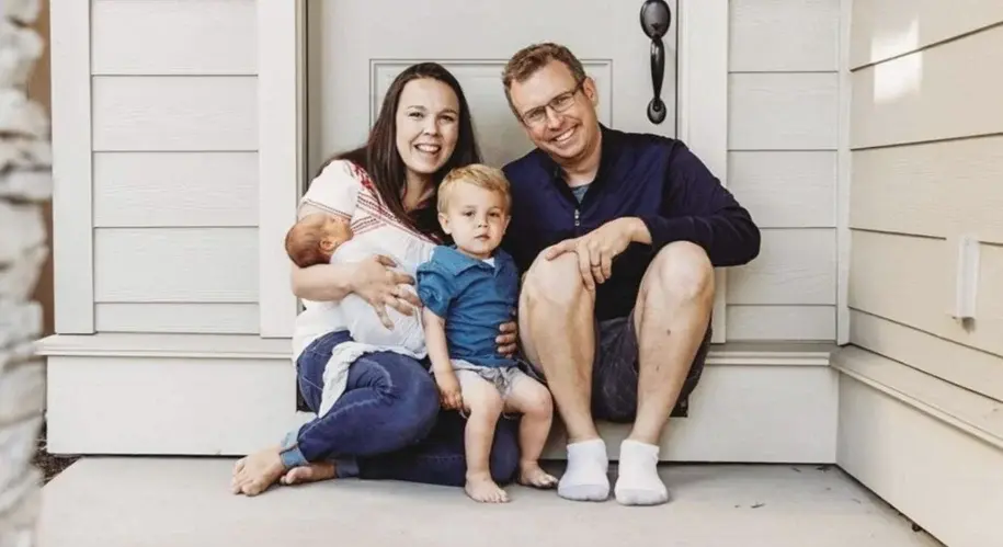 Smiling family with two young children sitting on the front porch of their home, enjoying time together