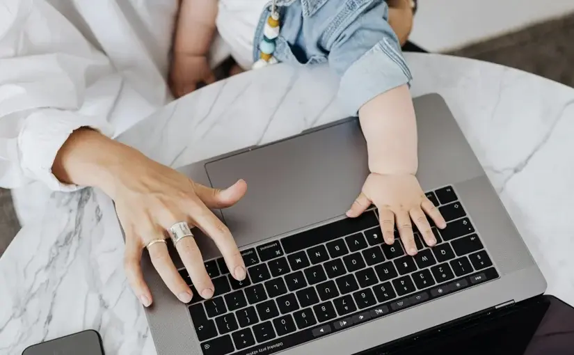 Child’s hand reaching toward a laptop keyboard while seated on a parent's lap, symbolizing work-life balance challenges