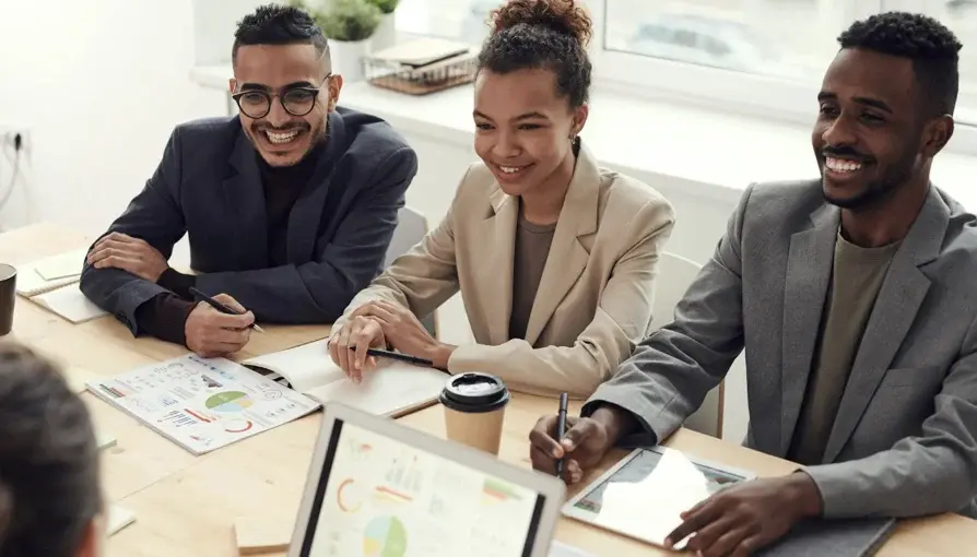 Three diverse professionals smile and engage during a collaborative meeting in an office setting.