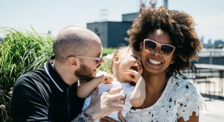 Couple smiling and holding their baby outdoors on a sunny day, enjoying a family moment