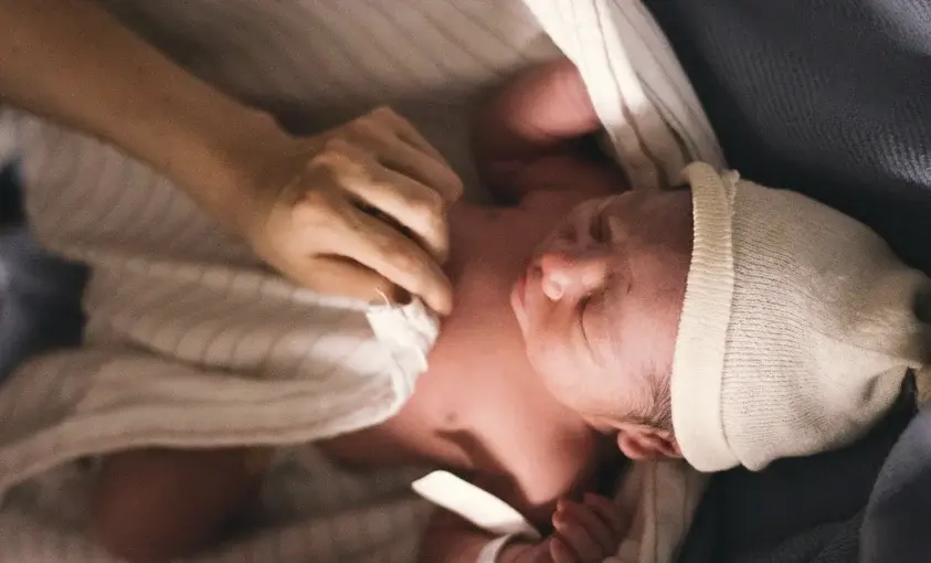 A tender close-up shows a person's hands gently touching a newborn baby's head.