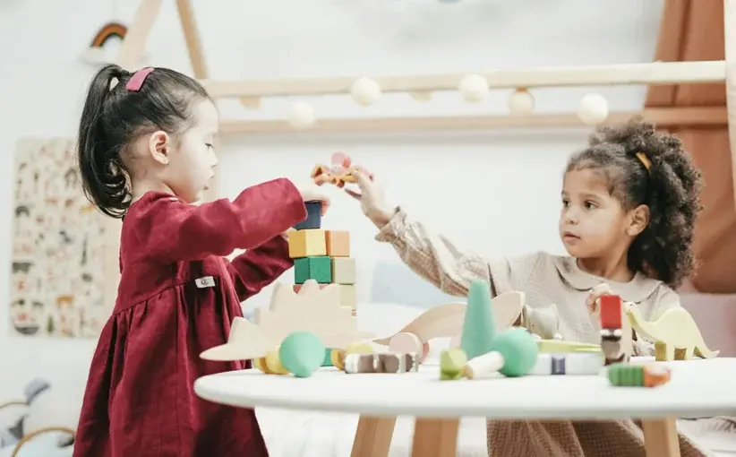 Two young girls are playing together with colorful wooden building blocks at a small table.
