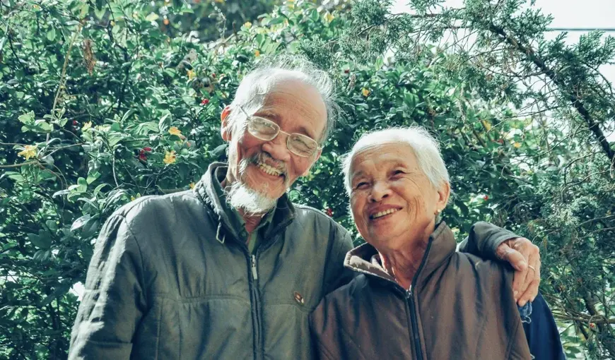 Elderly couple standing outdoors with arms around each other, smiling and enjoying a moment together