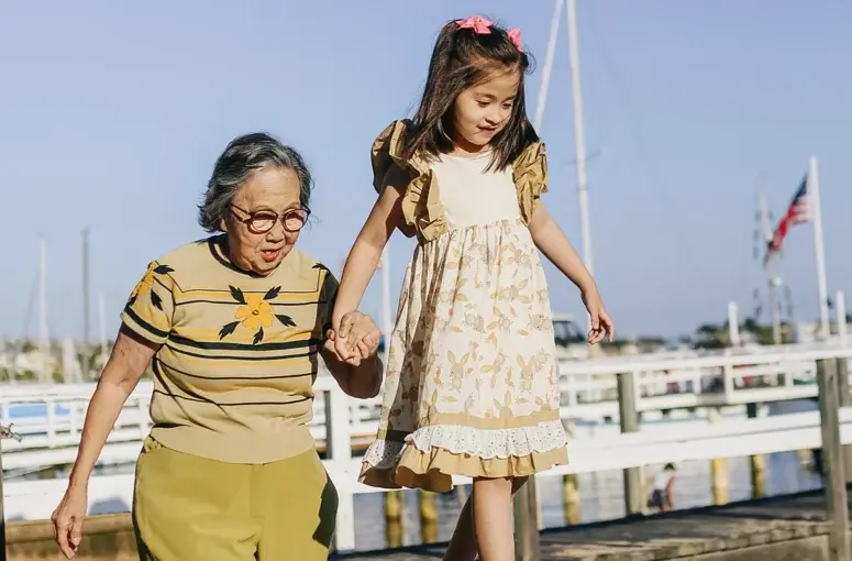 An elderly woman and a young girl holding hands and walking happily outdoors.