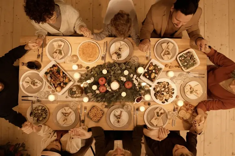 An aerial view of a group of people gathered around a festive dining table adorned with various dishes, drinks, and lit candles, creating a warm and inviting atmosphere.