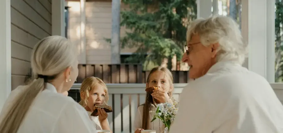 Two seniors and two children sitting around a table outdoors, sharing a meal and conversation together