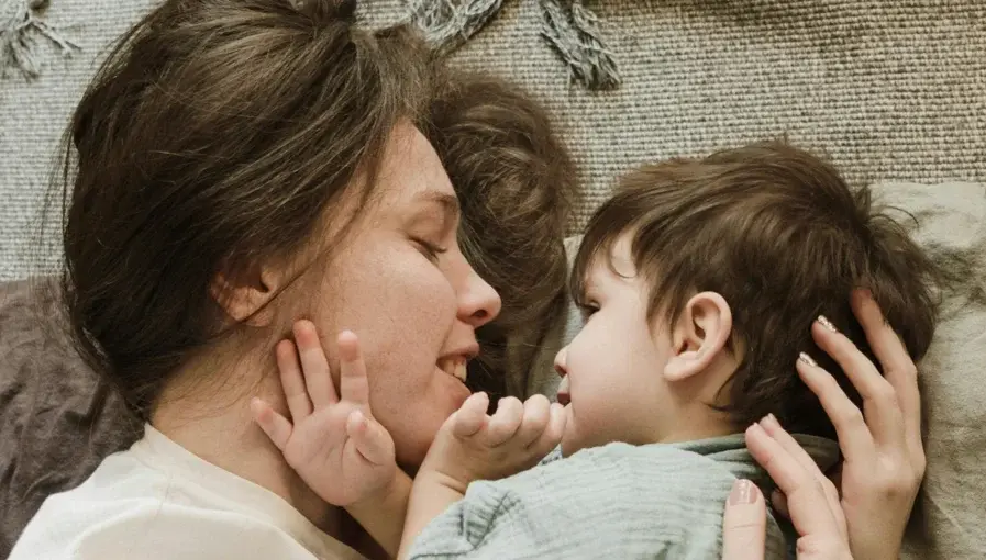 Mother and toddler lying face to face on a carpet, sharing a tender and affectionate moment