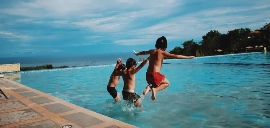 Two children jumping into a swimming pool on a sunny day.