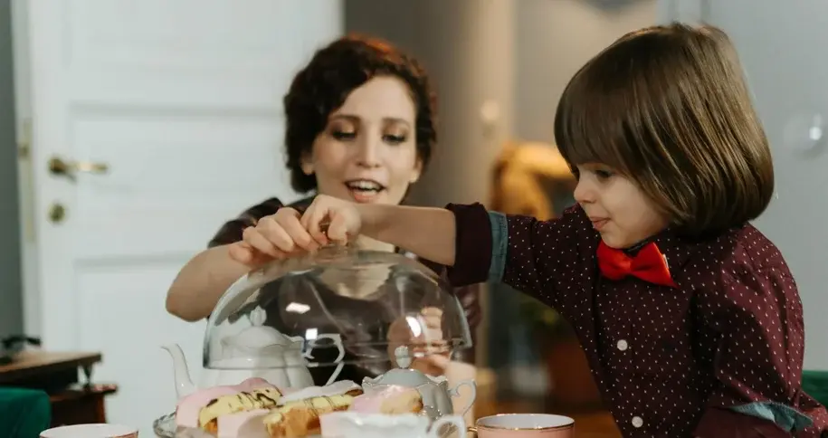 Woman and young boy decorating cupcakes together at a table, sharing a joyful and interactive moment