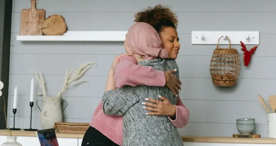 Two women embracing in a bright kitchen, sharing a supportive hug