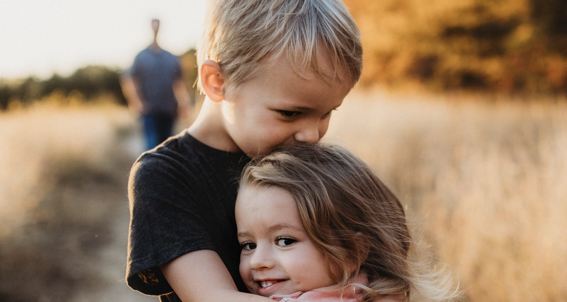 Older brother child kissing his younger sister on the head as she smiles