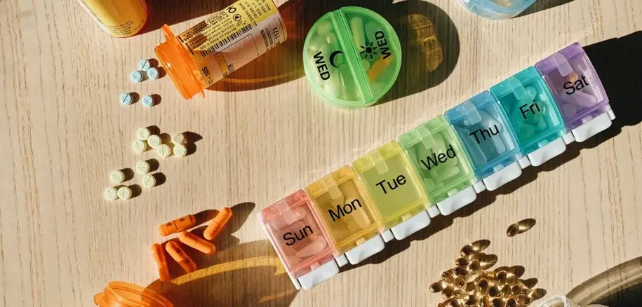 A seven-day pill organizer filled with various medications and capsules on a wooden table.