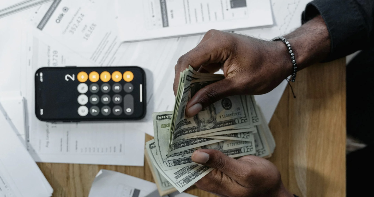 Man flipping through bills with a calculator on his phone as he budgets