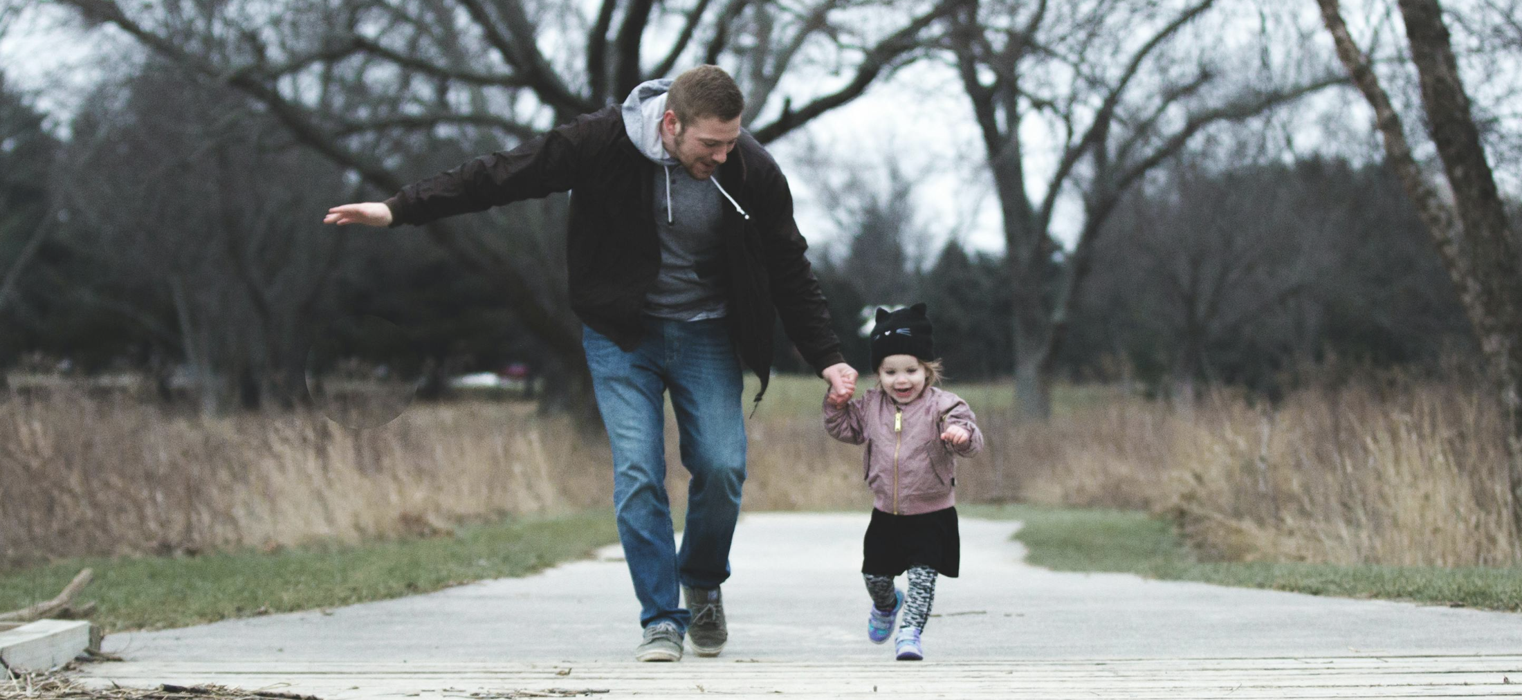 father holding his young daughters hand as the run down a path together 