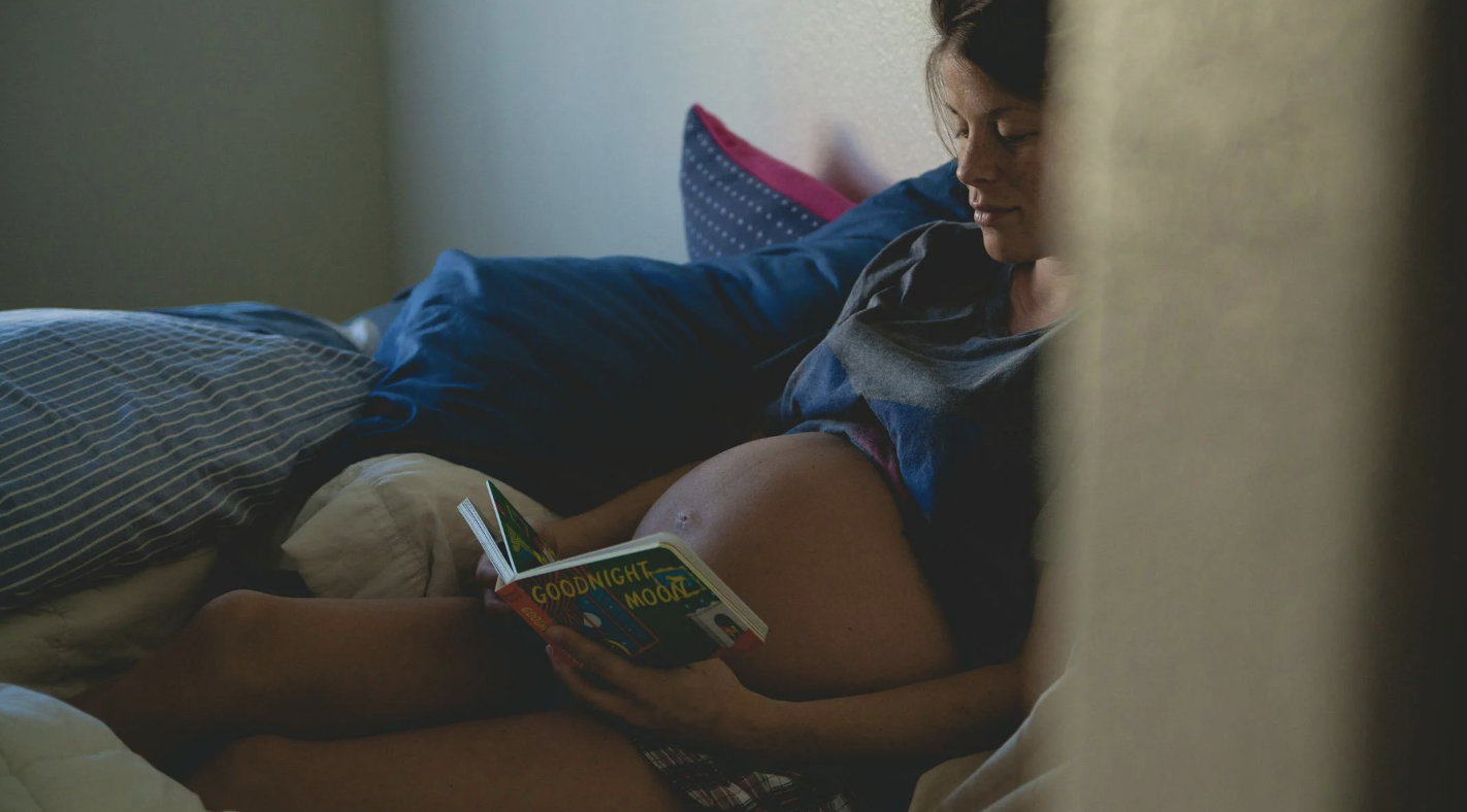 pregnant woman reading a children's book to her baby