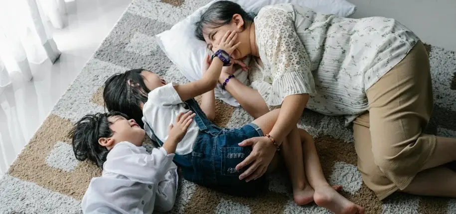 Mother lying on the floor with her two children, smiling and playing together in a relaxed home environment
