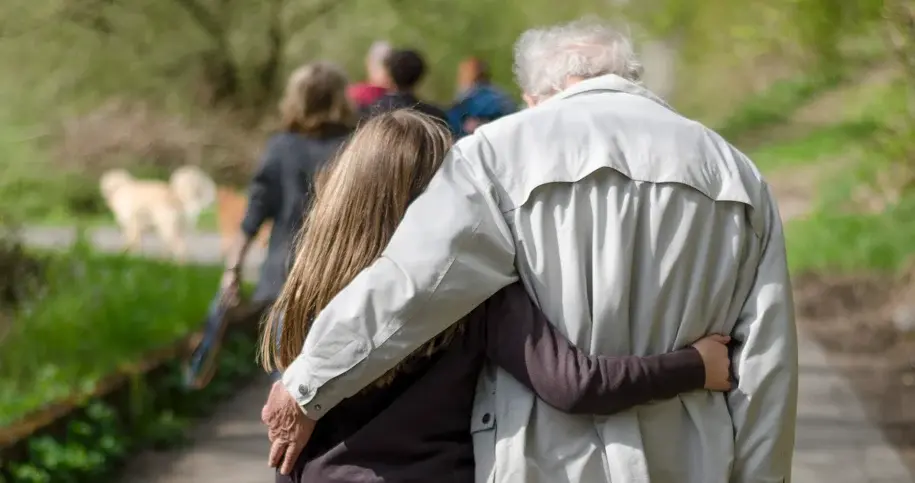 Adult walking arm-in-arm with an elderly parent along a path, symbolizing support and intergenerational care