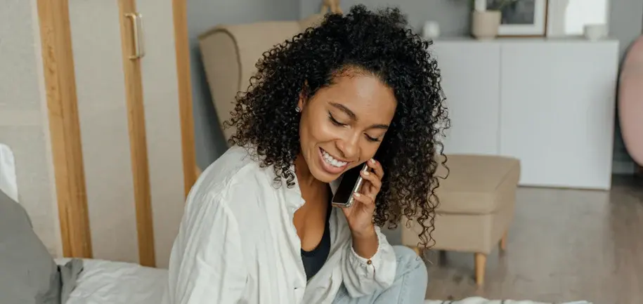 Smiling woman sitting on a couch while talking on the phone, appearing engaged and friendly during a conversation