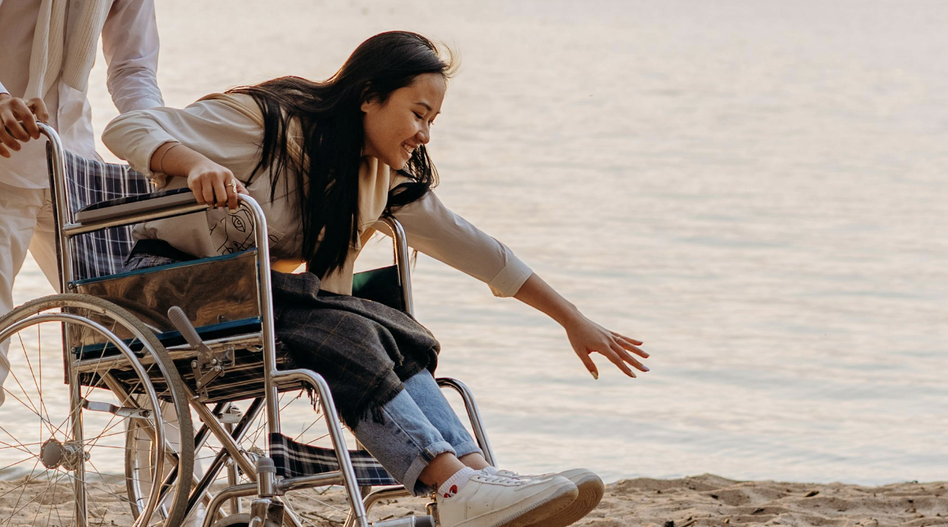 woman at the beach in a wheelchair being pushed by her care provider 