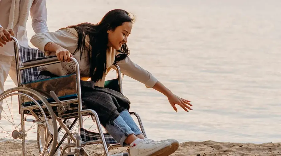 Caregiver playfully pushing a person in a wheelchair along the beach, both smiling and enjoying the moment