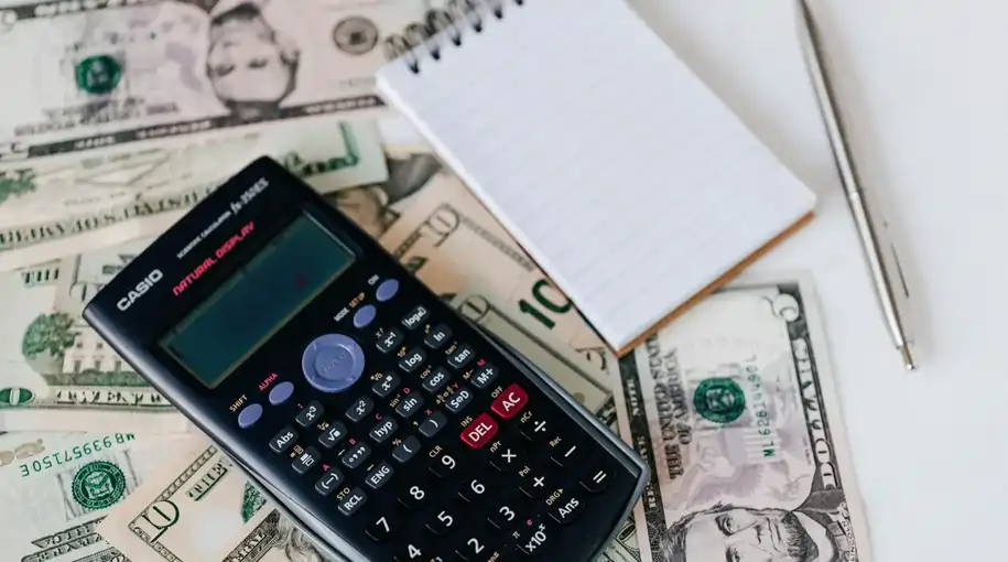 Calculator, notebook, pen, and dollar bills on a table, symbolizing financial planning and budgeting