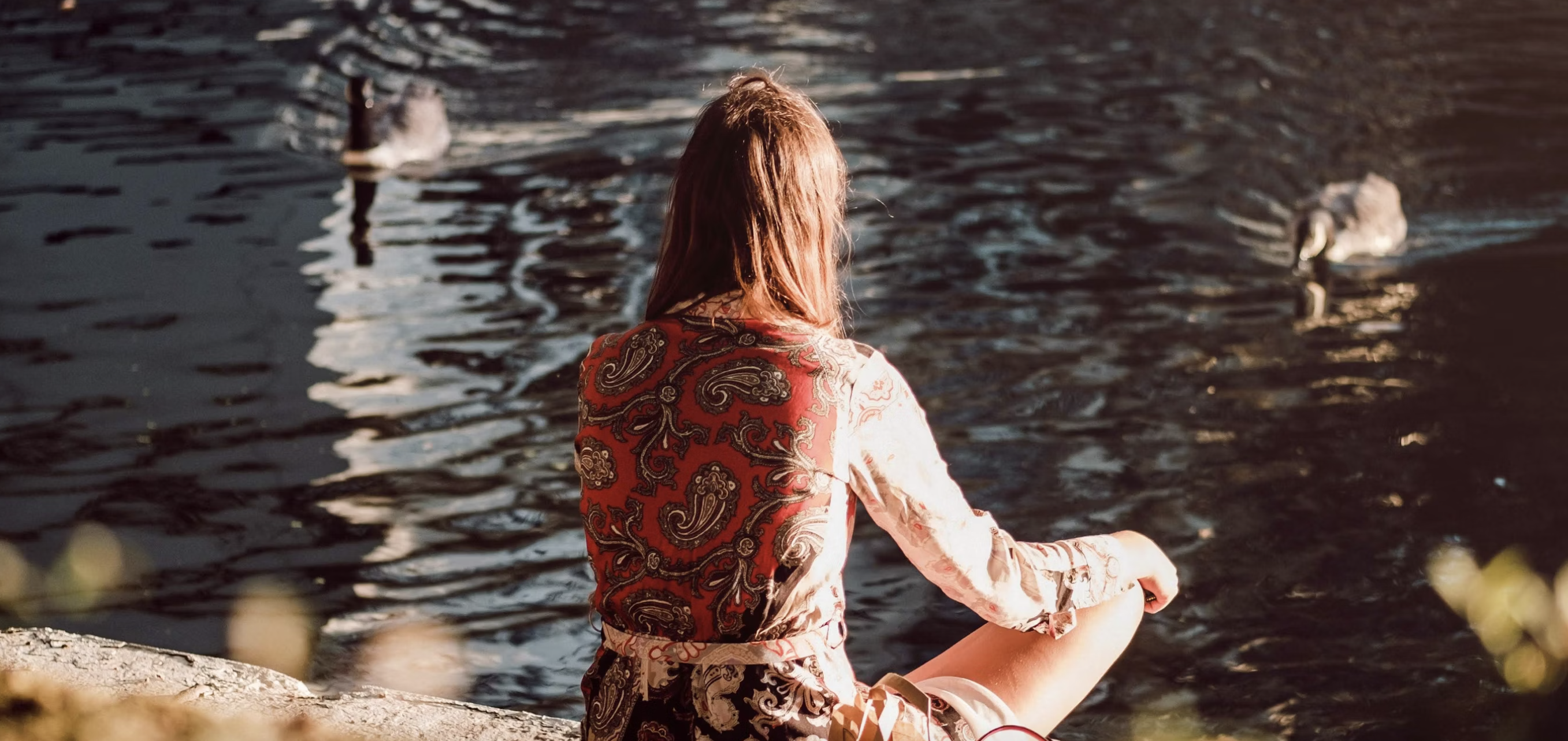 woman sitting beside a pond, feeding and admiring the swimming ducks