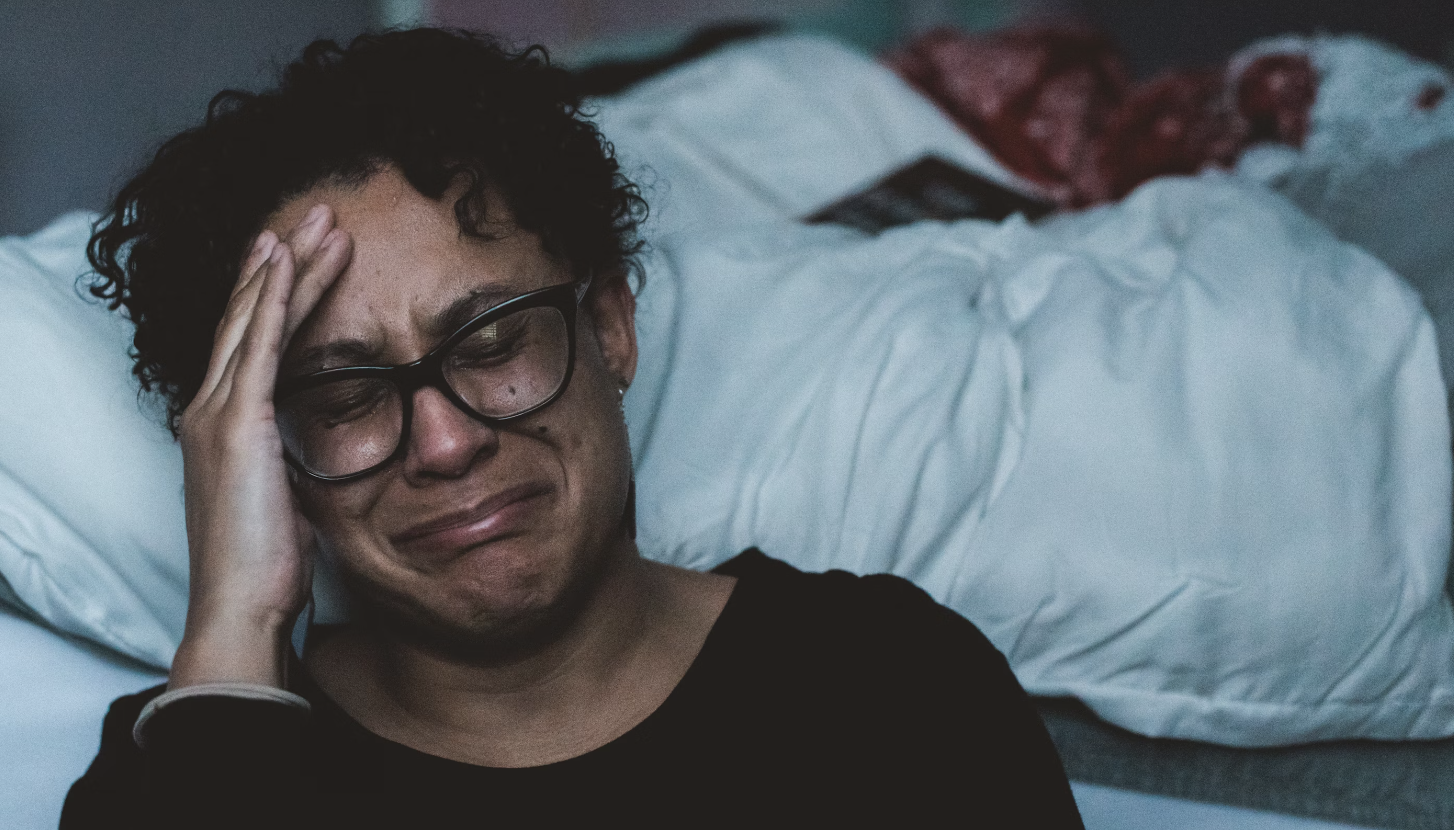 man leaning against his bed, sitting on the ground and crying