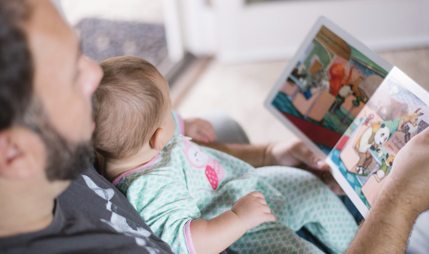 father reading a picture book to his baby on the couch 