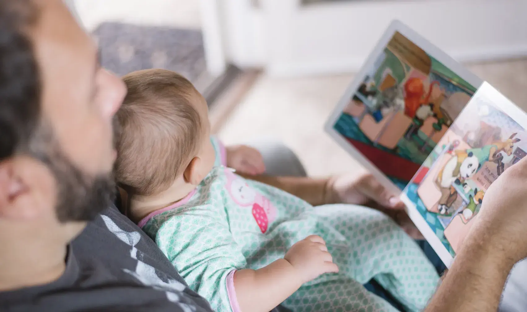 father reading a picture book to his baby on the couch