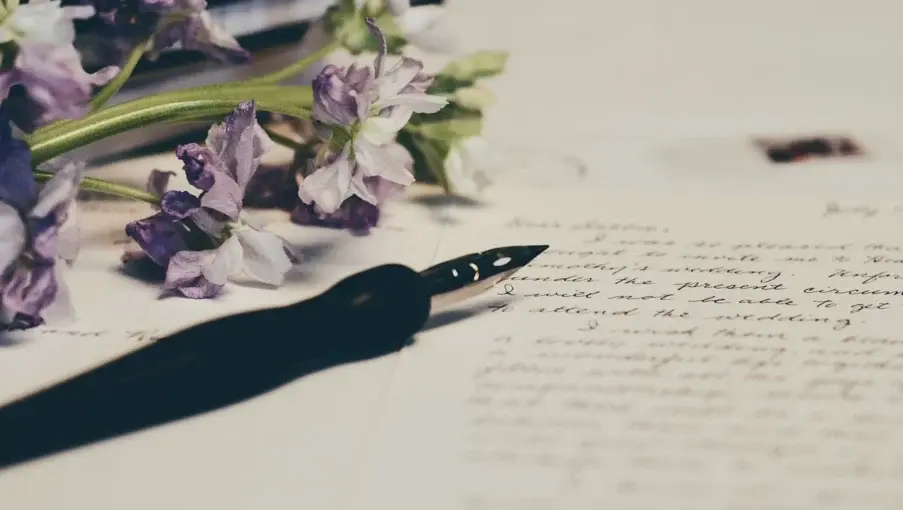 Handwritten letter on a table next to a fountain pen and a bouquet of purple flowers, symbolizing support and cared