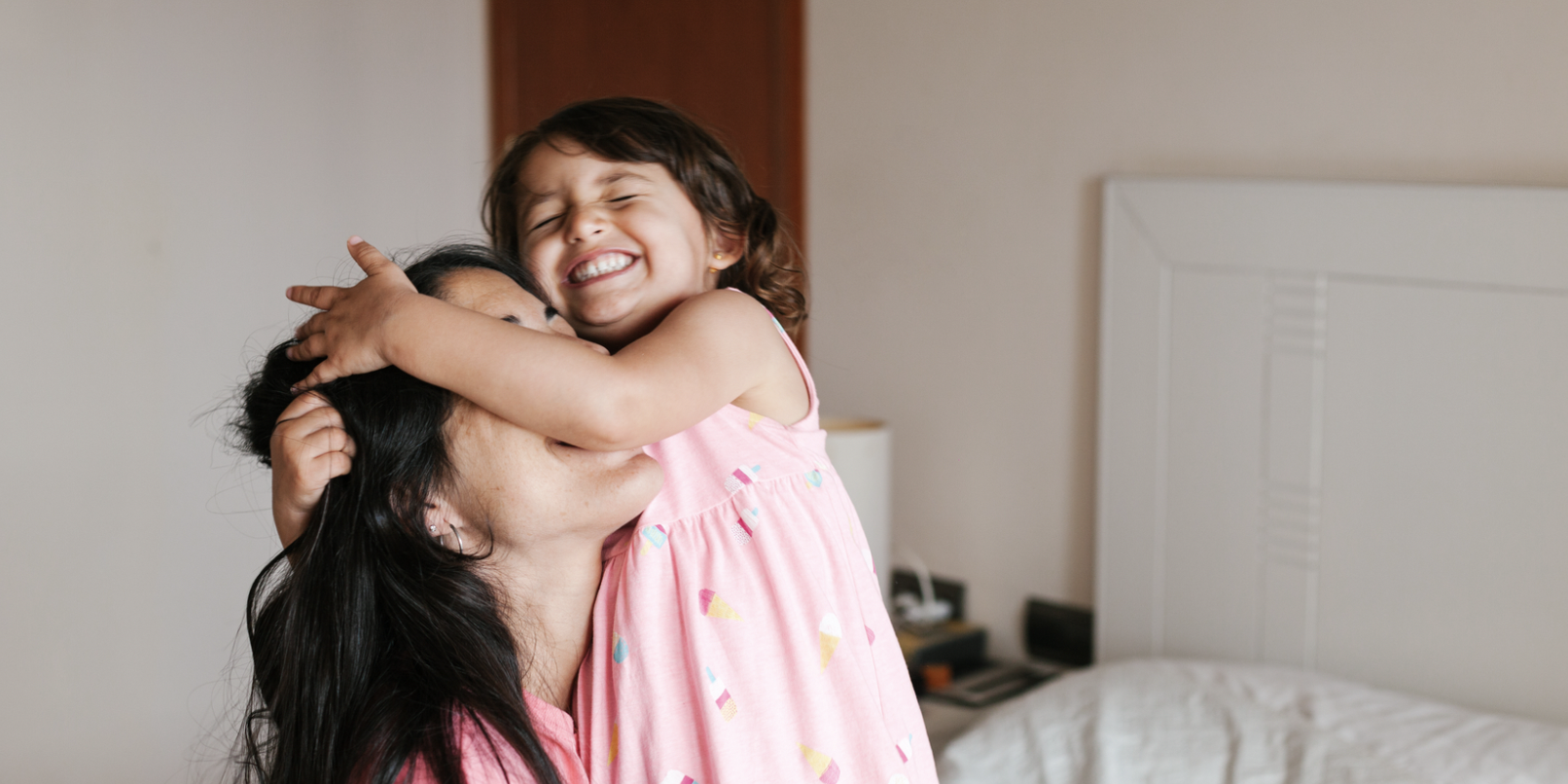 Daughter hugging her mom's face on the bed