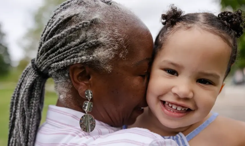 Elderly woman affectionately embracing a smiling young girl outdoors, showing a moment of joy and connection